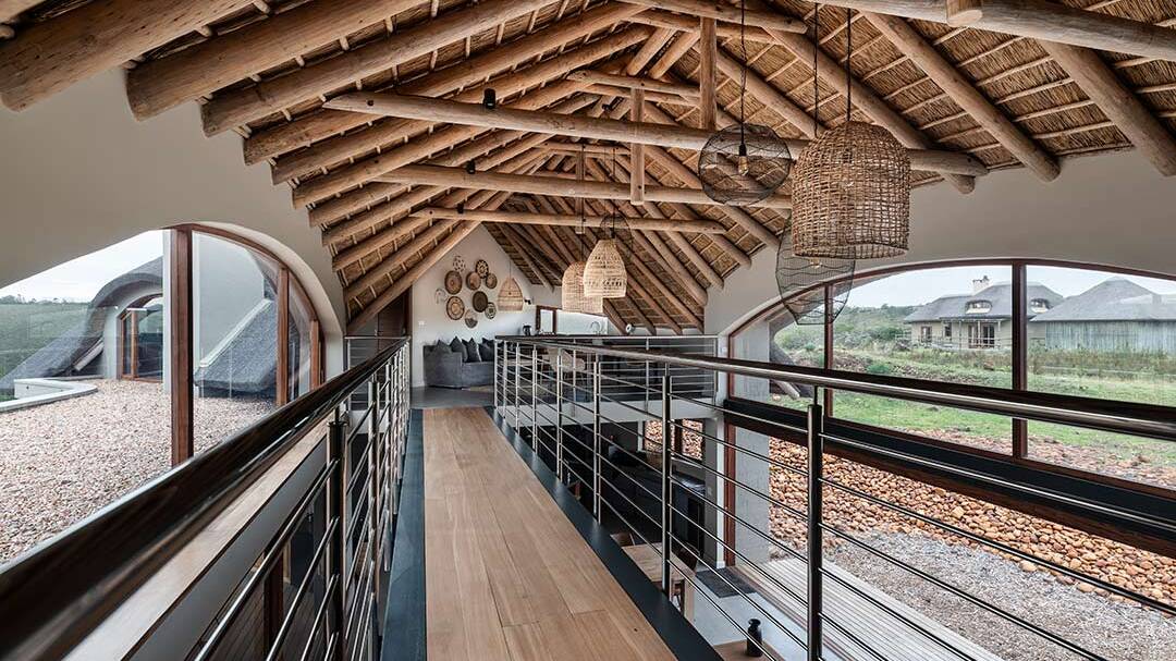 Mezzanine bridge beneath thatched rafters with woven pendants and long landscape windows