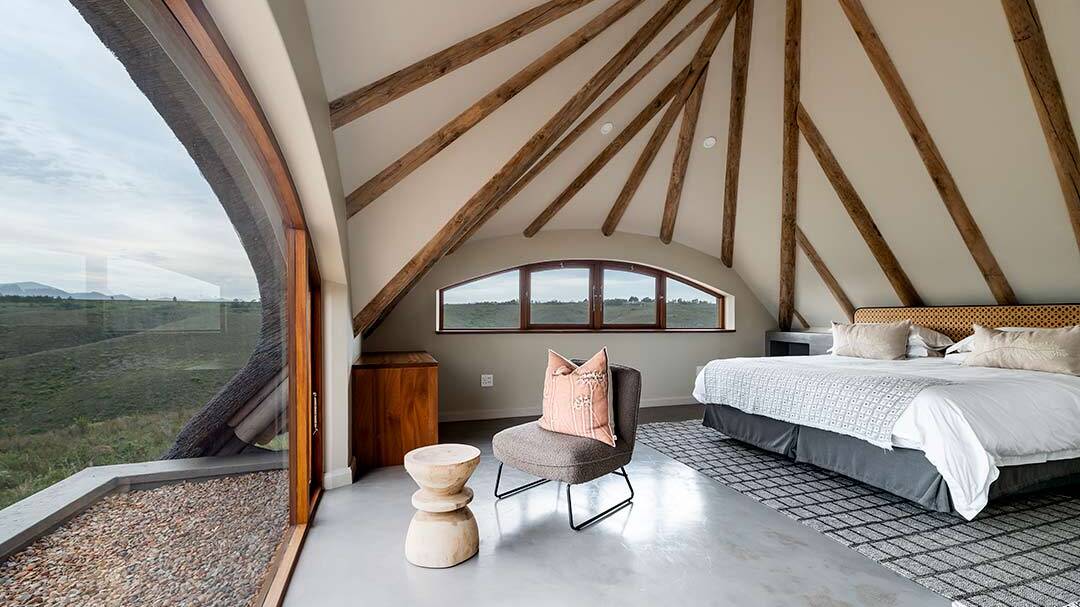 Loft bedroom under thatched roof with exposed timber rafters and curved dormer window