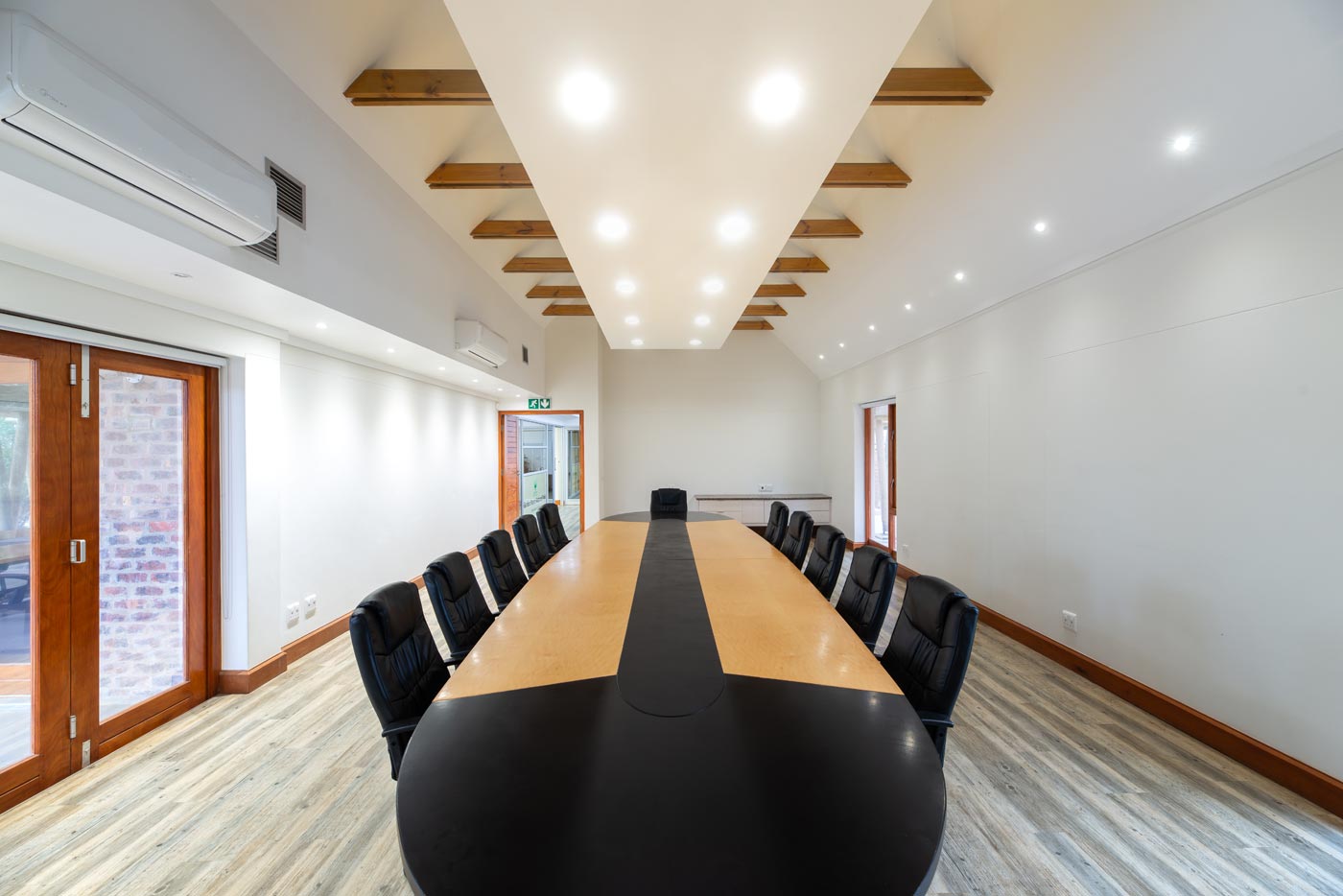 Central view of boardroom under illuminated raft ceiling with timber doors.