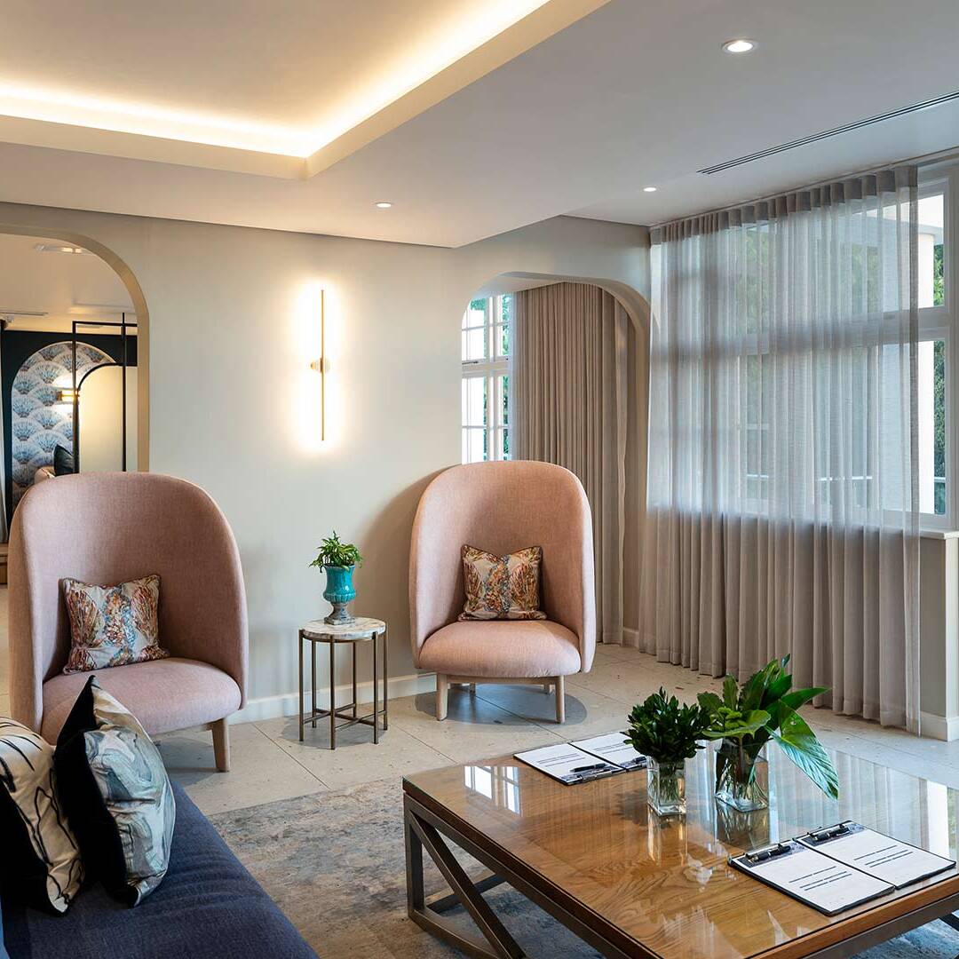 Daylit waiting lounge with pink wing chairs opening to terrace