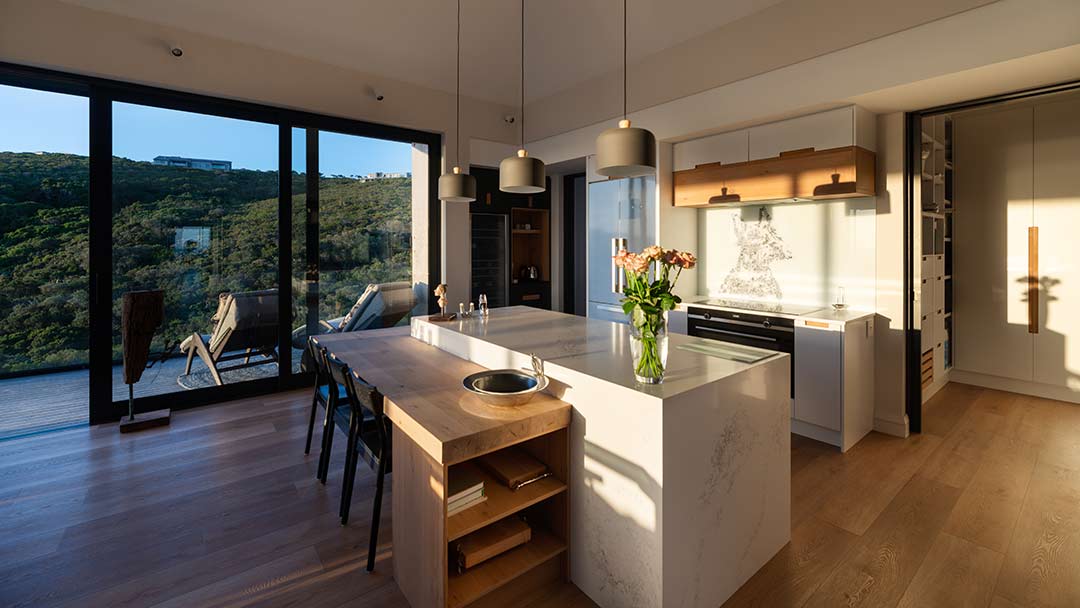 Kitchen with island and timber breakfast table opening to deck and coastal views, House 1418