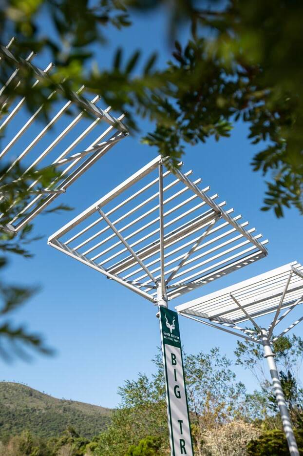 Close view of steel shade structures framed by foliage at the entrance plaza